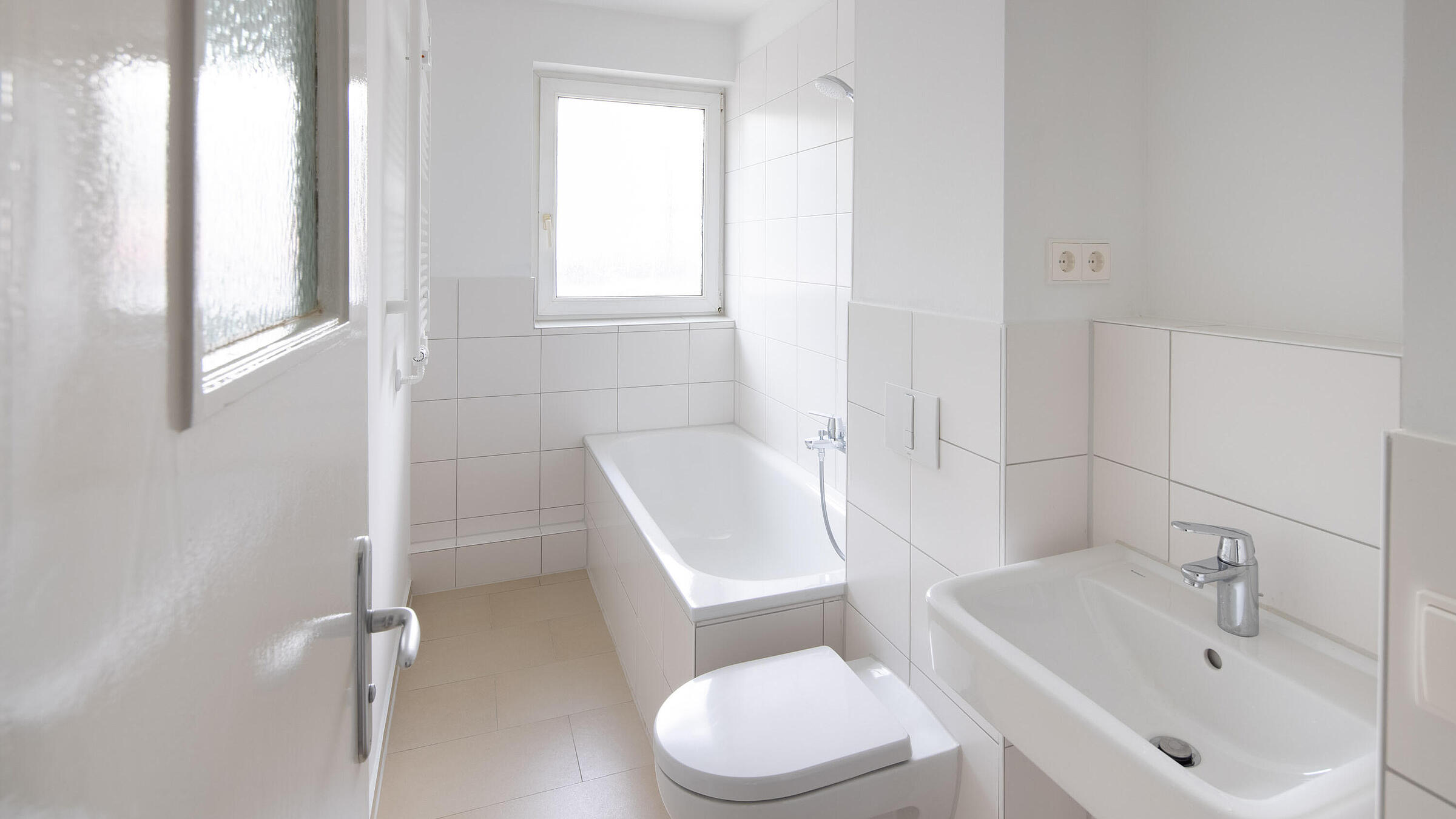Innenaufnahme zeigt ein modern gefliestes Badezimmer mit Waschbecken, WC und Badewanne.