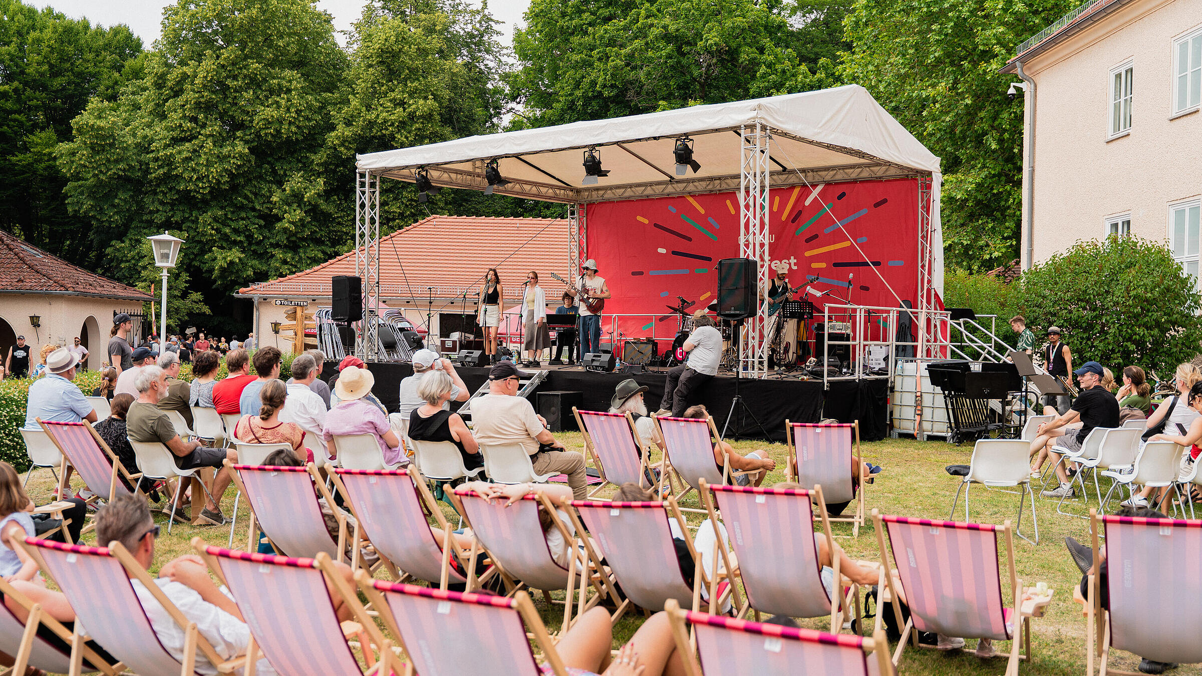 Weitwinkelaufnahme des Auftritts der Band allanwhy auf der Kleinen Bühne beim Kunstfest Pankow, im Vordergrund Menschen auf Sonnenstühlen.