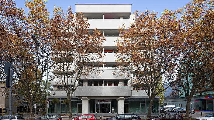 Bild zeigt Frontantsicht des neu gestalteten Wohn- und Geschäftsgebäudes im Wilhelmsruher Damm 142, Außenaufnahme. Im Vordergrund Bäume und parkende Autos.