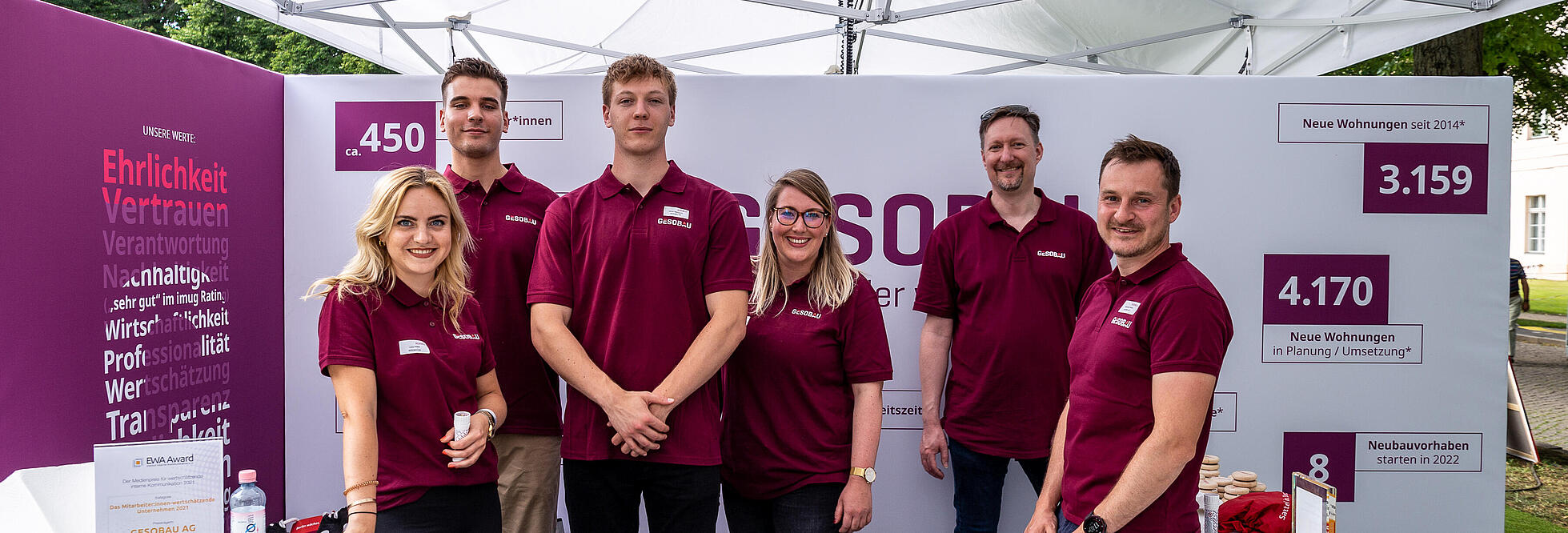 Außenaufnahme zeigt eine Gruppe Mitarbeiter*innen der GESOBAU in einheitlichen Poloshirts, die vor einem Messestand stehen.