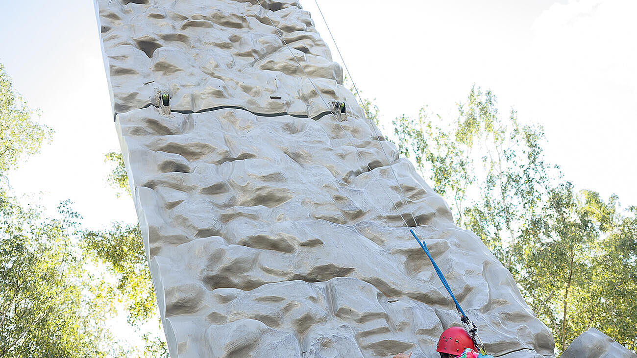 Perspektivaufnahme zeigt den Kletterfelsen von unten aus gesehen mit einem kletternden Kind.