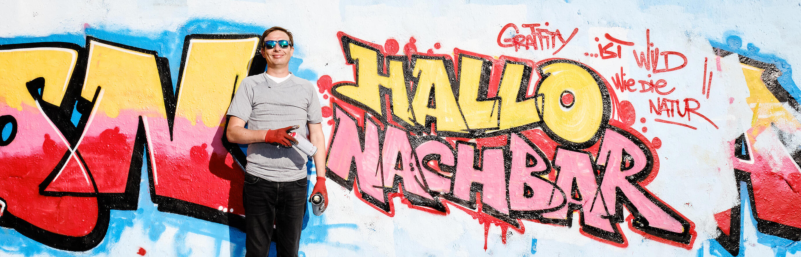 Außenaufnahme zeigt Jurij Pederin vor seinem "Hallo Nachbar"-Graffiti.