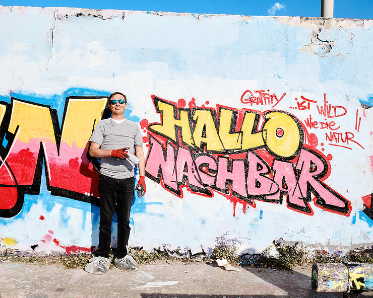 Außenaufnahme zeigt Jurij Pederin vor seinem "Hallo Nachbar"-Graffiti.