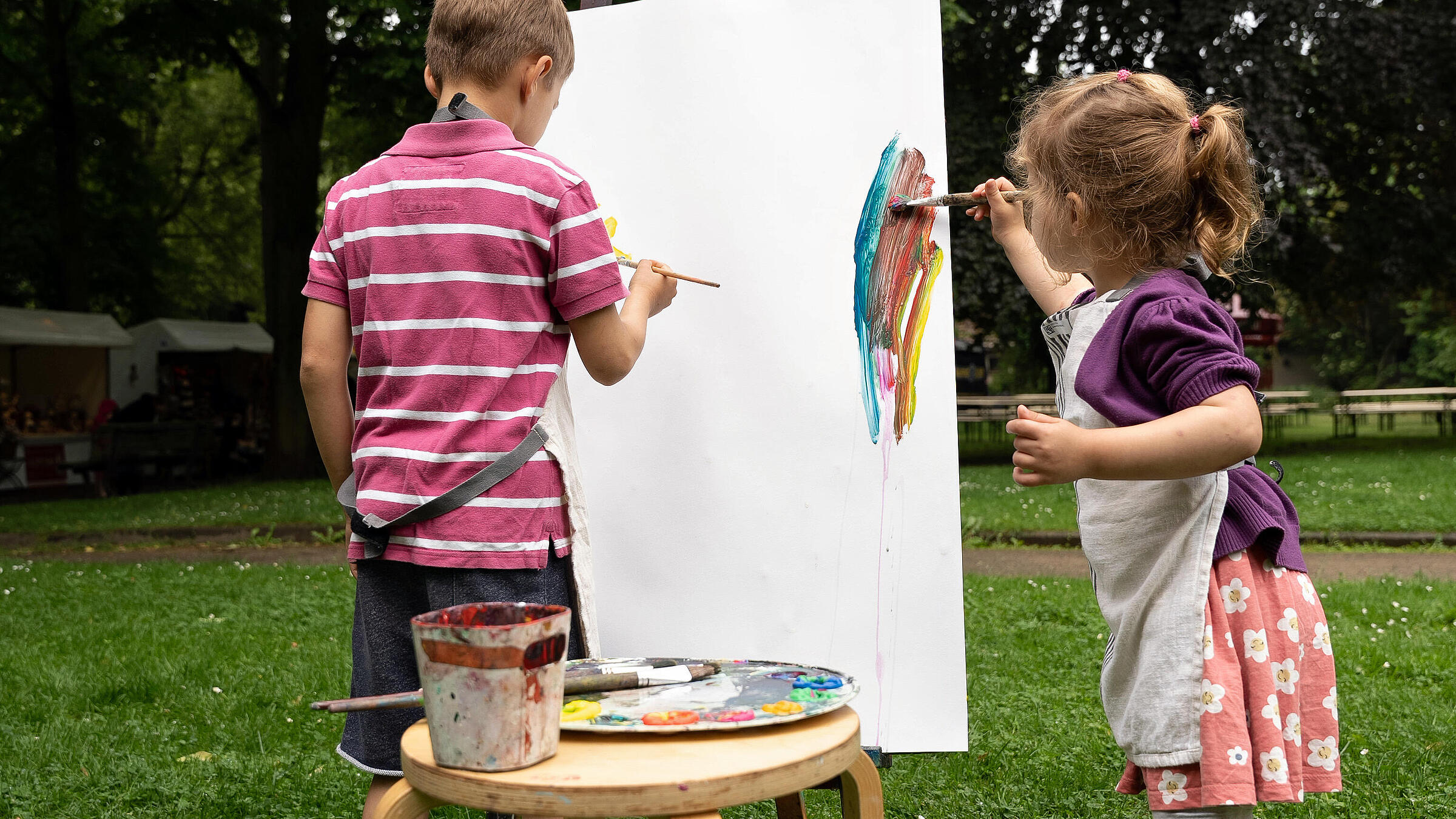 Außenaufnahme zeigt Kinder beim Bemalen einer Leinwand