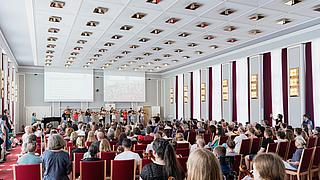 Blick in einen Konzertsaal, voll besetzt mit einem Kinderorchester vorne auf der Bühne