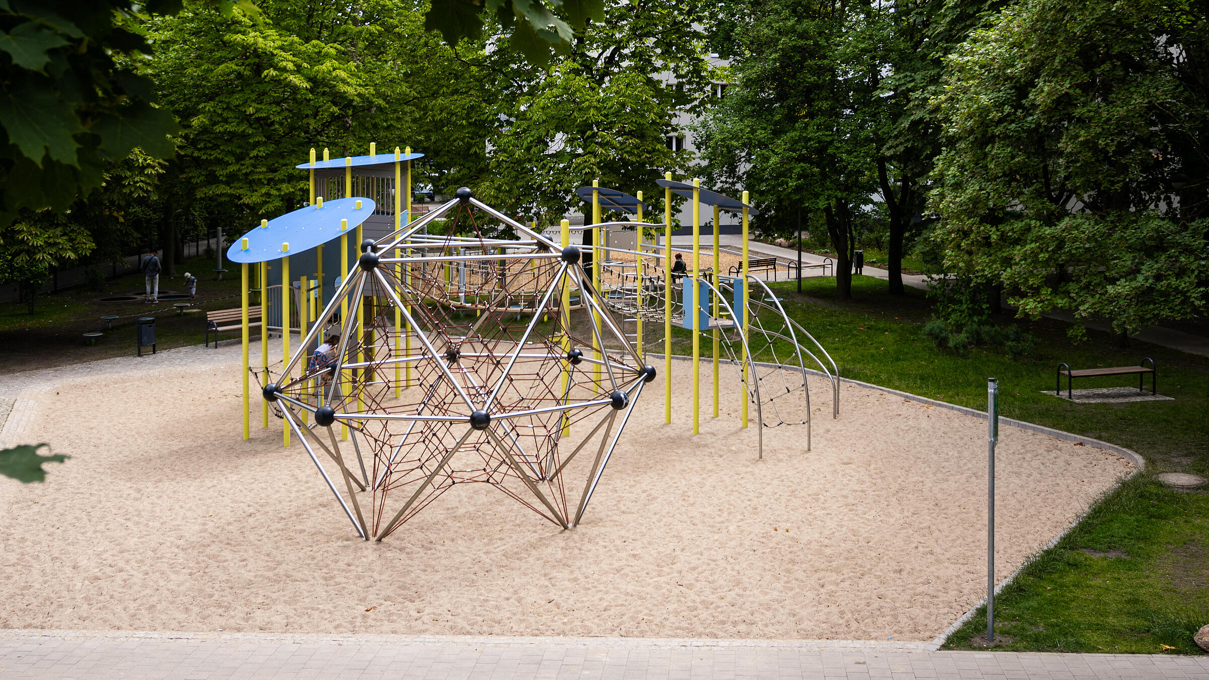 Außenaufnahme zeigt neuen Spielplatz am Eichhorster Weg, umgeben von Bäumen und Grünflächen. Im Hintergrund Wohnhaus.