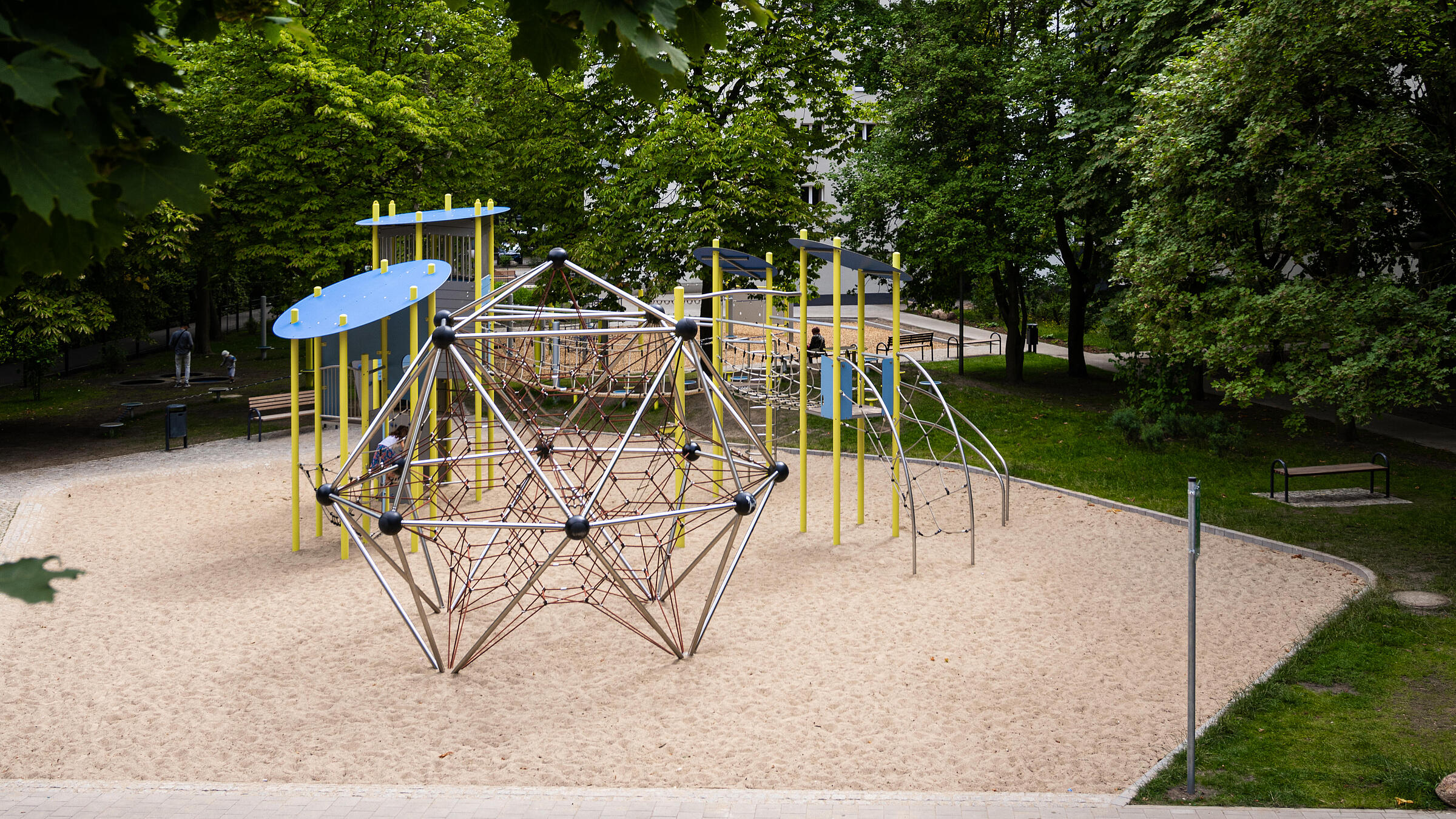 Außenaufnahme zeigt neuen Spielplatz am Eichhorster Weg, umgeben von Bäumen und Grünflächen. Im Hintergrund Wohnhaus.