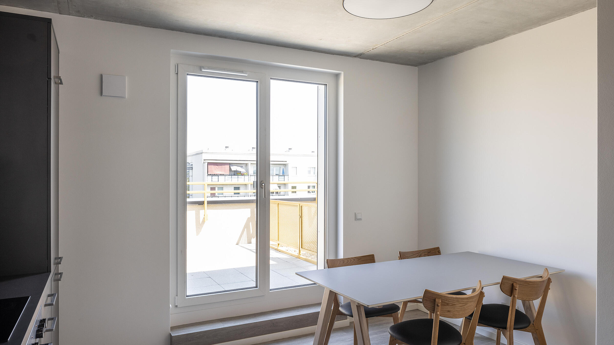 Innenaufnahme zeigt eine Wohnküche mit einem Tisch für vier Personen und Zugang zu einem Balkon.