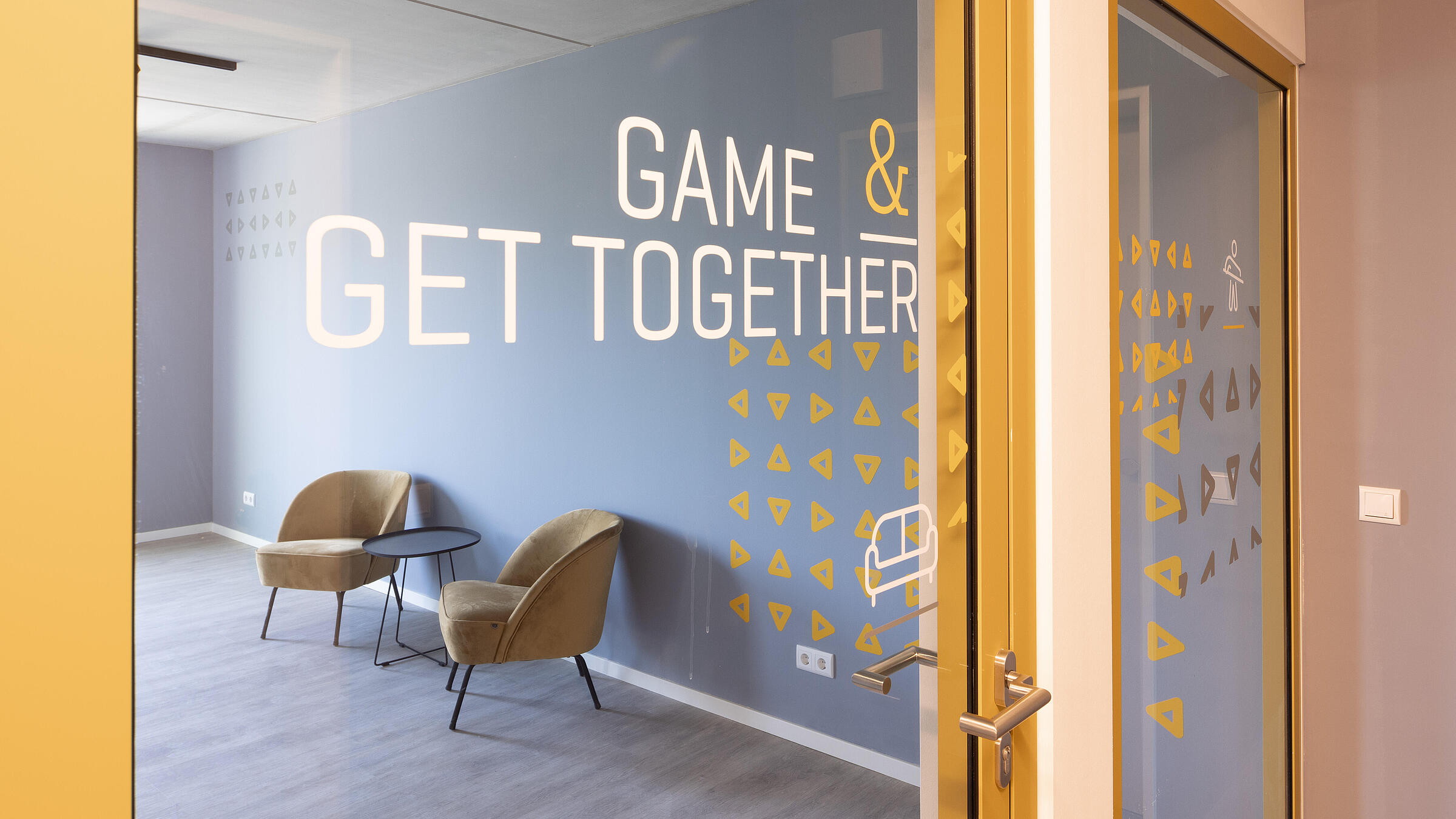 Innenaufnahme zeigt die Glastür zur Gemeinschaftsfläche "Game & Get Together".
